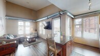 Located at 1880 Old Hudson Rd in Saint Paul, Minnesota, this single-floor unit blends modern finishes with distinct industrial-loft character. Exposed metallic ductwork runs throughout the living and kitchen areas, adding an urban edge to the otherwise warm, neutral-toned interior. Rich hardwood flooring flows seamlessly across the main living spaces, grounding the open-concept design.

The living room is bright and welcoming, with multiple windows that invite abundant natural light and offer views of the surrounding neighborhood. Elevated ceilings in this space enhance the sense of openness and volume.

The kitchen is well-appointed with warm cherry cabinetry, dark granite countertops, stainless steel appliances including a refrigerator, range, microwave, and dishwasher, and a central island with bar seating — ideal for casual dining and entertaining. Track lighting overhead keeps the space well-lit and functional.

The bedroom features the same soaring ceiling height found throughout, with large windows, exposed ductwork, and a generous closet. The bathroom is finished with matching granite and cherry cabinetry, hardwood-style flooring, and a full tub-shower combination. Overall, the space offers a cohesive, urban-inspired aesthetic with quality finishes throughout.