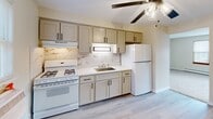 Located at 6946 W 65th St in Chicago's Bedford Park neighborhood, this single-floor unit offers two bedrooms, one bathroom, and a kitchen across a compact but efficiently laid-out floor plan. The living area features neutral beige carpeting, baseboard heating, and a large window that brings in natural light. The kitchen is outfitted with gray shaker-style cabinetry accented with matte black hardware, a marble-style tile backsplash, white gas range, and a full-size refrigerator, all complemented by light wood-look flooring and a ceiling fan overhead. The spacious primary bedroom is carpeted and features two large sliding-door closets with warm wood paneling, offering ample storage. A second bedroom, also carpeted, includes dual windows and baseboard heating, making it a comfortable and well-lit space. Ceiling fans are present throughout the unit, supporting climate control alongside the baseboard heating and window air conditioning units. The bathroom is finished with warm earth-tone tile on both the floors and walls, a tub-shower combination with a curtain, a wood-paneled vanity with a white basin sink, and a wall-mounted mirror. The overall aesthetic is clean, neutral, and functional.