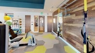 Located at 650 E Stonewall St. in Charlotte, NC, this contemporary fitness center is thoughtfully designed to support a full range of exercise disciplines across a single, well-appointed floor. The space is divided into distinct functional zones, each finished with a striking hexagonal-patterned carpet in tones of gray, taupe, and chartreuse that adds visual energy underfoot.

The main cardio and strength training area is anchored by floor-to-ceiling windows that flood the room with natural light and frame views of the surrounding Charlotte cityscape. A bold teal ceiling accentuates the open volume of the space, while a cable machine, stair climber, elliptical, and treadmills provide a comprehensive cardio and resistance training setup.

A dedicated functional training room houses an AbSolo core training machine, resistance equipment, stability balls, and wall-mounted accessories, all accessible through warm wood-framed doorways that provide architectural continuity throughout.

Adjacent to this is an open-plan yoga and group fitness studio with light hardwood-style flooring, a ceiling fan, and built-in shelving for props and equipment. Decorative artwork and rich wood accent walls contribute to an inviting ambiance. The space also benefits from direct outdoor terrace access, with large glass doors opening to views of the surrounding urban neighborhood, enhancing the sense of connectivity to the outdoors.