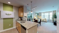 This well-appointed single-floor residence offers a thoughtfully designed open-concept layout connecting the kitchen, dining, and living areas. The kitchen is equipped with stainless steel appliances, including a refrigerator, range, and built-in microwave, complemented by warm maple cabinetry, granite countertops, and a peninsula island with pendant lighting overhead. Large-format tile flooring runs throughout the kitchen and entry areas, while recessed and track lighting provide ample illumination.

The living room is bathed in natural light from oversized windows with views of surrounding greenery, accented by soft neutral carpeting and warm-toned walls. A decorative glass partition with typographic design elements visually separates the living and dining spaces while maintaining an open feel.

The two bedrooms offer a serene retreat, each featuring plush carpet, large windows with blinds, and generous wall space. The bathroom includes a full soaking tub and shower combination with decorative tile surrounds, a vanity with wood cabinetry, and large-format floor tiles in a neutral taupe palette. The entryway features a mirrored closet and clean white millwork, contributing to the unit's cohesive, contemporary aesthetic.