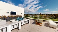 Located at 414 Front St in Santa Cruz, California, this rooftop terrace offers a sophisticated outdoor retreat with stunning panoramic views of the surrounding cityscape and distant mountain ranges. The terrace features a contemporary design defined by clean lines, smooth large-format tile paving, and crisp white stucco architecture.

The outdoor living area is thoughtfully arranged with multiple seating zones, including a generous sectional sofa, accent lounge chairs in bold yellow and teal, and a wall-mounted flat-screen television — creating a comfortable, resort-like atmosphere ideal for both relaxing and entertaining. Lush planters filled with ornamental grasses and flowering perennials add vibrant color and texture throughout the space.

A standout feature of the rooftop is the integrated green roof section, planted with a diverse mix of low-growing groundcovers and mulched beds, reflecting a commitment to sustainable design. Transparent glass panel railings line the perimeter, ensuring unobstructed sightlines across the Santa Cruz skyline while maintaining an open, airy feel. The terrace receives abundant natural light throughout the day, enhancing the overall ambiance. Large glass sliding doors connect the outdoor terrace to the interior, offering seamless indoor-outdoor flow and further maximizing the breathtaking views this elevated space provides.