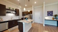 This single-floor residence offers a thoughtfully designed layout that balances modern style with everyday functionality. The kitchen serves as the heart of the home, showcasing rich dark cabinetry, granite countertops, and a full suite of stainless steel appliances including a refrigerator, range, and microwave. A central island with a granite surface provides additional prep space and casual seating, while pendant lighting above adds a refined touch. Classic white subway tile backsplash ties the space together with a clean, contemporary aesthetic. Warm hardwood-style flooring flows throughout the main living areas, enhancing the open and airy feel of the space. The kitchen opens naturally toward the entryway, which features a crisp white paneled door and generous ceiling height that contributes to a sense of openness throughout. The bathroom is well-appointed with a granite-topped vanity, dark cabinetry consistent with the kitchen's design language, a soaking tub with shower combination, and hardwood-style flooring. The bedroom is generously sized with plush carpeting and corner windows that invite abundant natural light and outdoor views, creating a calm and restful retreat. Overall, the space presents a cohesive modern design with quality finishes throughout.
