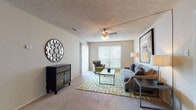 This single-floor residence offers a thoughtfully designed layout that balances comfort and functionality across its key living spaces. The living room serves as the heart of the home, featuring plush carpeting, a ceiling fan with light fixture, and a large window with vertical blinds that invites natural light and outdoor views. The room provides generous space for seating and entertaining, with a warm, neutral color palette throughout.

Adjacent to the living area, the kitchen is finished with dark espresso cabinetry, granite-style countertops, a tile mosaic backsplash, and hardwood-style flooring. The galley configuration maximizes counter and storage space, and includes a stainless steel electric range, dishwasher, and sink. A breakfast bar peninsula connects the kitchen to the dining area, which comfortably accommodates a full dining set.

The residence includes two bedrooms, each carpeted and equipped with ceiling fans, window blinds for privacy, and ample space for bedroom furnishings. The bathroom is finished with matching dark cabinetry, granite-style countertops, hardwood-style flooring, and a shower-tub combination. Consistent finishes and a neutral tone throughout the home create a cohesive, move-in-ready atmosphere.