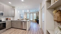 This thoughtfully designed one-bedroom, one-bathroom unit offers a functional and modern layout across a single floor. The open-concept living and kitchen area serves as the heart of the space, featuring light-toned hardwood-style flooring that flows throughout. The kitchen is equipped with gray shaker-style cabinetry, granite countertops, a subway tile backsplash, and a full suite of stainless steel appliances, including a refrigerator, range, microwave, and dishwasher. A kitchen island with pendant lighting adds both prep space and a visual anchor to the room. The living area benefits from large windows and a sliding glass door that invite abundant natural light, complemented by a ceiling fan overhead. The entryway hallway features a built-in mudroom-style nook with shelving, hooks, and a bench, providing practical storage. The bedroom is carpeted and receives natural light through a window, with access to a dedicated closet. The bathroom includes granite countertops, gray cabinetry, a tub-shower combination with tile surround, and hardwood-style flooring, maintaining a cohesive, contemporary aesthetic throughout the unit.