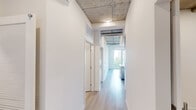 Located at 201 The Promenade N in Long Beach, CA, this two-bedroom, one-bathroom residence blends industrial character with modern finishes across a single thoughtfully designed floor. The space is defined by its striking exposed concrete ceilings with visible ductwork and conduit, creating an authentic loft aesthetic complemented by clean white walls and light wood-look flooring throughout.

The kitchen is a standout feature, showcasing a large waterfall-edge quartz island with an undermount sink and a professional-style faucet. Sage-toned cabinetry with gold hardware is paired with stainless steel appliances, a subway tile backsplash, and pendant lighting, all framed by floor-to-ceiling windows that bring in abundant natural light.

The primary bedroom is generously proportioned, offering a dedicated closet and direct access to the hallway. Both bedrooms feature the signature exposed concrete ceilings, wide-plank flooring, and roller shade windows that filter natural light. A ceiling fan adds comfort to one of the rooms.

The bathroom is finished with warm wood-look tile flooring and tub surround, a grey vanity with gold hardware, built-in shelving, and a sliding glass shower enclosure. Two hallways connect the space efficiently, and a dedicated closet provides additional storage. The overall ambiance is airy, modern, and distinctly urban.