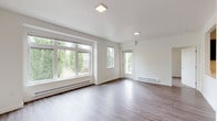 Located at 4255 Maple Street SE in Olympia, Washington, this single-floor unit presents a clean, contemporary design throughout. The open-concept living area is anchored by wide-plank hardwood-style flooring and crisp white walls, creating a bright and cohesive atmosphere. Large windows along the living room wall flood the space with natural light and frame views of surrounding greenery, while a glass-panel door provides access to an outdoor area.

The kitchen is thoughtfully designed with dark espresso cabinetry extending to the ceiling, white countertops, and a full suite of stainless steel appliances including a refrigerator, range, microwave, and dishwasher. A pass-through opening connects the kitchen to the main living area, reinforcing the open flow of the layout.

The bedrooms feature neutral carpet and windows overlooking the outdoors, offering a quiet, comfortable retreat. Two bathrooms serve the unit: one includes a combination tub and shower with built-in shelving and hardwood-style flooring, while the other features a sleek vanity with a white countertop, dark cabinetry, and a wide mirror. Baseboard heating is present throughout, and the overall design maintains a consistent modern aesthetic.