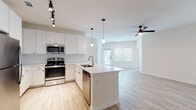 This single-floor residence is designed with a contemporary aesthetic, emphasizing open-concept living and a cohesive, neutral color palette. The kitchen serves as a central hub of the space, outfitted with white shaker-style cabinetry, a classic subway tile backsplash, and a full suite of stainless steel appliances including a refrigerator, range, microwave, and dishwasher. A peninsula with a built-in sink and light countertop extends into the living area, providing additional workspace and a natural gathering point. Pendant lighting and a track light fixture illuminate the kitchen, adding both function and style.

The open living area flows seamlessly from the kitchen, featuring light hardwood-style flooring, a ceiling fan, and a glass-paneled door that invites natural light from outside. The generous layout offers flexibility for various furniture arrangements.

The bedroom is carpeted for comfort and includes a walk-in closet with built-in shelving, accompanied by a window that brings in natural light. The bathroom is finished with white subway tile surrounding the soaking tub and shower combination, complemented by brushed gold fixtures, wood-style flooring, and white cabinetry for a clean, modern look.