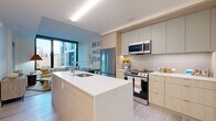Located at 44 M St NE in Washington, DC, this modern one-bedroom, one-bathroom residence offers a well-appointed, single-floor layout with contemporary design throughout. The open-concept living and dining area is anchored by expansive floor-to-ceiling windows that frame sweeping urban views and flood the space with natural light, creating an airy, connected atmosphere. The kitchen is a standout feature, showcasing a large waterfall-edge island with an undermount sink, light wood flat-front cabinetry, quartz countertops, a textured tile backsplash, and stainless steel appliances including a gas range and built-in microwave. Light wood-tone flooring flows seamlessly throughout the unit. The bedroom is a serene retreat with generous proportions, wall-to-wall glazing with sliding access to an outdoor balcony, and dedicated closet space. The bathroom is clean and refined, featuring a wood-vanity with quartz countertop, a glass-enclosed walk-in shower with rain showerhead, and marble-style tile flooring. A dedicated closet provides additional storage. The overall aesthetic is modern and neutral, with a warm palette that complements the vibrant NoMa neighborhood surrounding the residence.