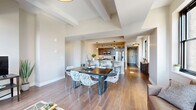 Located at 90 State Street in the heart of downtown Albany, NY, this well-appointed 2-bedroom, 3-bathroom residence offers a thoughtfully designed open-concept layout with contemporary finishes throughout. Rich hardwood flooring flows seamlessly across the living, dining, and kitchen areas, anchored by elevated ceilings with architectural beam detailing that adds a sense of spaciousness and character.

The kitchen is a standout feature, equipped with stainless steel appliances including a gas range and French door refrigerator, dark espresso cabinetry, and a large center island with quartz countertops, pendant lighting, and bar seating — ideal for both cooking and entertaining. The open dining area connects naturally to the living room, where large black-framed windows frame sweeping views of the Albany skyline and fill the space with natural light.

Both bedrooms are generously proportioned, each featuring hardwood floors, large windows with urban views, and a calm, neutral palette. The primary bedroom is notably spacious and well-suited as a private retreat. The three bathrooms are cleanly finished, with one showcasing a glass-enclosed walk-in shower with subway tile surround and mosaic tile flooring. Additional bathrooms offer tile flooring and city-facing windows. The overall ambiance is modern, bright, and urban.