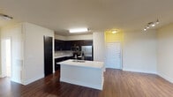 Located at 2416 Fort Worth Ave in Dallas, TX, this single-floor unit offers a thoughtfully designed open-concept layout that seamlessly connects the kitchen and living areas. The kitchen is a standout feature, showcasing rich dark cabinetry that extends to the ceiling, a subway tile backsplash, stainless steel appliances including a French door refrigerator and built-in microwave, and a central island with a white countertop and undermount sink — ideal for both meal prep and casual dining. Dark hardwood-style flooring runs throughout the main living areas, providing a warm and cohesive aesthetic. The spacious living room benefits from multiple windows fitted with horizontal blinds, allowing natural light to fill the space, while a ceiling fan adds comfort and functionality. An arched doorway leads toward additional rooms, adding an architectural touch to the interior. The bedroom is generously proportioned, featuring plush carpeting, a ceiling fan, and a trio of windows that invite abundant natural light. The bathrooms are finished with dark wood vanities, white countertops, tiled tub-and-shower combinations, and hardwood-style flooring, maintaining a consistent design language throughout. The entry foyer provides a clean transition into the open living space, completing this well-appointed unit.