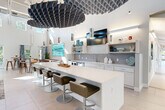 Located at 89 Hopkins Street in Wakefield, MA, this expansive single-floor amenity space offers a thoughtfully designed environment spanning nearly 3,000 square feet. The layout includes four living areas, a dedicated exercise room, and a connecting hallway, all finished with contemporary materials and a cohesive coastal-inspired color palette.

The main lounge is a showpiece, featuring soaring ceilings, abundant natural light from oversized windows, and an eye-catching floor-to-ceiling white brick fireplace with a mounted flat-screen TV. Teal accent chairs, modern pendant lighting, and a foosball table give the space a lively yet comfortable atmosphere. A wet bar area is conveniently situated nearby.

The indoor-outdoor transition area is particularly noteworthy, with wide folding glass doors that open fully to a covered outdoor terrace. Here, a substantial stone-surround fire pit table serves as a central gathering point, surrounded by stylish seating and views of the landscaped grounds.

The fitness center is well-equipped with treadmills, ellipticals, cycling machines, cable systems, and a full dumbbell rack. The room benefits from high ceilings, exposed ductwork, ceiling fans, large mirrors, and bold graphic wall art, creating an energizing workout environment.

The entry hallway is bright and welcoming, with teal accent walls, light hardwood-style flooring, and glass-windowed private offices. The exterior features natural stacked stone cladding and manicured green landscaping.
