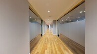 Located at 205 Church Street in the heart of New Haven, CT, this well-appointed fitness facility spans a generous single floor and is organized into four distinct exercise rooms, each designed to serve a specific training purpose. A sleek, light-filled corridor with warm hardwood flooring and full-length glass partition walls connects the spaces, creating an open and transparent flow throughout the facility. The first exercise room functions as a dedicated studio space, featuring polished hardwood floors, floor-to-ceiling mirrors, and an assortment of free weights including dumbbells, kettlebells, and stability balls — ideal for group classes or personal training sessions. A second room is outfitted with cardio equipment, including treadmills, elliptical machines, and a stationary bike, all positioned beneath recessed lighting with natural light filtering in through street-facing windows. A third room is dedicated to strength training, housing a variety of plate-loaded machines and cable systems on durable rubber flooring, with windows providing natural light and ventilation. The fourth room completes the circuit with additional free weights, a multi-station cable machine, and mirrored walls. Recessed lighting throughout ensures consistent, well-lit conditions across all areas, and the overall design reflects a clean, modern aesthetic suited for a professional fitness environment.