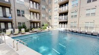 This single-floor residence is part of a multi-story building complex centered around a striking outdoor pool area. The courtyard pool is framed by the building's neutral-toned façade with private balconies overhead, and is lined with lounge chairs and a seating area with cushioned furniture, creating an inviting outdoor retreat.

Inside, the open-concept layout connects the living and kitchen areas seamlessly. The kitchen is outfitted with dark espresso cabinetry reaching toward the ceiling, stainless steel appliances including a refrigerator, electric range, microwave, and dishwasher, light stone countertops, a classic white subway tile backsplash, and wood-look flooring. Track lighting above adds a modern touch.

The living area offers a comfortable, open space with wood-look flooring, a ceiling fan, and bright white walls that create a clean, airy atmosphere.

The bedrooms feature plush carpeting, ceiling fans, and walk-in closets, providing practical storage. The bathroom includes dark cabinetry with a white countertop vanity, wood-look flooring, and a full tub-shower combination, maintaining the unit's consistent design palette throughout.