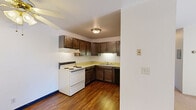 Located at 218 Royal Ct in Fox Crossing, Wisconsin, this two-bedroom, one-bathroom unit offers a practical single-floor layout designed for comfortable everyday living. The kitchen features dark wood cabinetry, light countertops, hardwood-style flooring, and an electric range with an overhead ventilation hood, providing a functional and organized cooking space. The living room is carpeted and bright, with a ceiling fan and a sliding glass door that opens to a private outdoor balcony, allowing natural light and outdoor views to enhance the space. Baseboard heating and wall-mounted air conditioning units are present throughout, ensuring year-round comfort. The primary bedroom is generously sized with plush carpet, a window overlooking the surrounding greenery, and an expansive set of bifold closet doors offering ample storage. The second bedroom is also carpeted and includes its own bifold closet. The bathroom is divided into two areas — a vanity space with a white cabinet, mirror, and sink, and a separate wet area with a tub-shower combination. Warm-toned wood doors and neutral wall colors are consistent throughout, giving the space a cohesive and understated aesthetic.