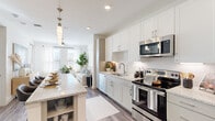 This single-floor residence is designed with a clean, contemporary aesthetic, characterized by a neutral palette of whites, grays, and warm wood tones that create a cohesive and inviting atmosphere throughout. Wood-style plank flooring runs consistently across the main living areas, adding warmth and visual continuity.

The kitchen serves as a central hub of the home, featuring white shaker-style cabinetry extending to the ceiling for ample storage, granite-look countertops, a textured tile backsplash, and a full suite of stainless steel appliances including a side-by-side refrigerator, electric range, and over-the-range microwave. A kitchen island with open shelving provides additional prep space and casual seating. The kitchen flows seamlessly into the living area, which benefits from large windows that invite abundant natural light and views of the surrounding area. A ceiling fan anchors the living space.

The bedrooms are comfortably scaled, each featuring large windows, plush carpeting, and ceiling fans. The bathroom offers a granite-topped vanity, wood-style flooring, white cabinetry, and a tiled soaking tub and shower combination, maintaining the home's consistent modern style.