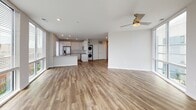 This single-floor residence offers a thoughtfully designed open layout that maximizes space and natural light throughout. The expansive living area is defined by floor-to-ceiling windows and sliding glass doors on two sides, framing sweeping urban skyline views and flooding the interior with daylight. Wood-style flooring runs throughout the main living spaces, complemented by crisp white walls and a ceiling fan that enhances airflow and comfort.

The kitchen is outfitted with white shaker cabinetry extending to the ceiling, a subtle tile backsplash, neutral quartz-style countertops, and a full suite of stainless steel appliances including a slide-in electric range, over-the-range microwave, and French door refrigerator. A peninsula provides additional prep and seating space, while a stacked washer and dryer unit is conveniently integrated nearby.

The bedrooms feature plush carpeting, natural light from single windows with blinds, and closet access. The primary bathroom includes a glass-enclosed walk-in shower, white vanity cabinetry, and a large mirror. The secondary bathroom offers a soaking tub and shower combination with tile surround, a matching vanity, and tile flooring, maintaining a clean, neutral aesthetic throughout.