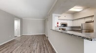 Located at 15100 Ella Blvd in Houston, TX, this single-story, 2-bedroom, 1-bathroom home offers a well-designed layout with consistent wood-look flooring and neutral gray tones throughout. The open living room is bathed in natural light through large windows with blinds and connects seamlessly to the kitchen via a pass-through counter, creating an airy, connected feel. Crown molding adds a refined touch to the living and bedroom areas.

The kitchen is well-appointed with white cabinetry, granite countertops, a double-basin sink, and a full suite of stainless steel appliances, including a range, microwave, and refrigerator. The spacious primary bedroom features mirrored sliding closet doors and a ceiling fan, while the second bedroom also includes a ceiling fan and a bright window with outdoor views. Both bedrooms offer generous proportions with clean, neutral finishes.

The bathroom includes a tiled tub-shower combination with a decorative accent stripe, complemented by a granite-topped vanity and wood-look flooring. An attached garage provides additional utility space and houses the in-unit washer and dryer hookups, offering practical everyday convenience. The overall ambiance is clean, modern, and move-in ready.