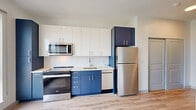 Located along the South Side waterfront in Pittsburgh, this modern studio unit offers a well-designed open-concept layout with contemporary finishes throughout. Light wood-tone flooring flows seamlessly across the entire space, creating a warm and cohesive aesthetic.

The kitchen is a standout feature, boasting a striking two-tone cabinet design with crisp white upper cabinets and bold navy blue lower cabinets, complemented by a white subway tile backsplash and stainless steel appliances — including a refrigerator, range, microwave, and dishwasher. A large picture window in the main living area floods the space with natural light and frames a picturesque view of the river and surrounding Pittsburgh hillside.

The bedroom area features a clerestory window that borrows light from adjacent spaces, maintaining a bright and airy atmosphere while offering a sense of privacy. A sliding closet door adds a clean, space-conscious touch.

The hallway connects the living spaces efficiently and includes a built-in utility panel. The bathroom is finished in a clean, minimalist style with light wood-look tile flooring, a white floating vanity with an undermount sink, and a mirror — creating a calm, functional space.

Overall, this unit presents a modern, efficient design with quality finishes, abundant natural light, and impressive waterfront views.