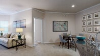 This single-floor residence offers a thoughtfully designed layout with distinct living spaces connected by a cohesive neutral color palette of warm beige tones, plush carpeting, and tile flooring. Crown molding accents the living and dining areas, adding a refined architectural detail throughout.

The living room is bright and welcoming, featuring large windows with French doors that invite natural light and provide outdoor access. A distinctive built-in arched shelving unit serves as a focal point, offering dedicated display and media space. Adjacent to the living area, the dining space accommodates a round table and seating, with a wainscoted accent wall and decorative framed artwork enhancing its character.

The galley-style kitchen is efficiently organized with white cabinetry, dark granite-style countertops, tile flooring, and a full suite of stainless steel appliances, including a range, microwave, refrigerator, and dishwasher.

The bedrooms are carpeted and comfortable, each offering natural light through window treatments and closet storage. The primary bedroom includes a walk-in closet. The bathroom features a white vanity with dark countertop, a large mirror, and tile flooring. A dedicated in-unit laundry room houses a full-sized washer and dryer with overhead shelving.