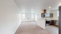 This single-floor residence features a clean, contemporary design characterized by bright white walls, neutral tones, and an efficient layout. The open-concept living area is generously proportioned, with plush wall-to-wall carpeting, recessed lighting, and multiple windows fitted with vertical blinds that allow natural light to fill the space. A wall-mounted HVAC unit serves the living area, adding practical climate control.

The kitchen is seamlessly integrated into the living space via a peninsula-style half-wall, creating an open flow ideal for entertaining. Dark espresso cabinetry contrasts handsomely with marble-patterned countertops, while stainless steel appliances — including a range, microwave, dishwasher, and refrigerator — complete the functional setup. A wall-mounted range hood and a window above the sink add both utility and light to the cooking area. Wood-look flooring in the kitchen transitions neatly to carpet in the living zone.

Multiple bedrooms each feature soft carpeting, white walls, and large windows with outdoor views. Two bathrooms are finished with wood-look flooring, marble-patterned vanity countertops, dark cabinetry, and a tub/shower combination, delivering a cohesive and modern aesthetic throughout.