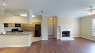 Located at 1200 Pickett Branch Rd in Cary, NC, this single-floor residence offers a thoughtfully designed open-concept layout with consistent warm-toned hardwood flooring throughout the main living areas. The spacious living room is a standout, anchored by a classic white-mantled fireplace and complemented by crown molding along the ceilings. A ceiling fan and large windows allow natural light to fill the space, with views of the surrounding community and pool area visible from one of the bedrooms.

The kitchen is efficiently designed with light wood cabinetry, granite countertops, and black appliances including a refrigerator, range, and built-in microwave. A pass-through counter connects the kitchen to the living and dining areas, enhancing the open flow of the space. Tile flooring in the kitchen provides a practical transition from the hardwood in the main areas.

The bathrooms are well-appointed, featuring granite-topped vanities with dual sinks, wood cabinetry with brushed hardware, and a combination shower and soaking tub. An arched hallway detail adds an architectural touch, lending character to the interior. The layout, as seen in the floorplan overview, includes multiple bedrooms, making this a comfortable and functional residence.