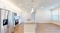 This single-floor, 2-bedroom, 2-bathroom residence offers a thoughtfully designed open-concept layout with modern finishes throughout. The kitchen serves as the centerpiece of the living area, anchored by a large island with granite countertops, an undermount sink, and stylish pendant lighting. White shaker cabinetry, a subway tile backsplash, and a full suite of stainless steel appliances — including a French door refrigerator, range, and microwave — complete the space. Wood-look flooring flows through the main living areas, complemented by crown molding and recessed lighting that enhance the clean, contemporary aesthetic. The open living area benefits from multiple windows with blinds, filling the space with natural light. Both bedrooms are carpeted and feature ceiling fans and windows with natural views, providing a comfortable, quiet retreat. Two dedicated closets offer ample storage. The bathrooms are finished with granite-topped white vanities, hardwood-style flooring, and tiled tub-shower combinations. The overall design is bright and cohesive, blending practical functionality with modern style in a well-organized floor plan.