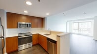 Located on the 7th floor at 180 Brookline Ave in Boston's Fenway neighborhood, Unit 701 is a well-appointed one-bedroom, one-bathroom residence offering a thoughtfully designed layout across a single floor. The open-concept kitchen and living area serves as the heart of the unit, where warm-toned wood cabinetry pairs with stainless steel appliances — including a refrigerator, range, built-in microwave, and dishwasher — and a light-colored quartz countertop with a marble-style tile backsplash. A peninsula counter provides a natural division between the kitchen and the living space, which features hardwood-style flooring throughout and a large picture window that fills the room with natural light and frames views of the surrounding cityscape. The bedroom is a comfortable, well-proportioned room with its own window overlooking the Boston skyline, hardwood-style flooring, and a dedicated closet for storage. The bathroom is clean and modern, finished with white tile, a soaking tub with shower, and warm wood vanity cabinetry. Recessed lighting throughout the unit adds a polished, contemporary feel to this functional urban residence.