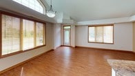This single-floor residence offers a thoughtfully designed layout that balances open living spaces with comfortable private quarters. The main living and dining area is defined by soaring vaulted ceilings and an abundance of natural light streaming through multiple large windows fitted with wood-framed blinds. Warm hardwood-style flooring flows throughout the main living areas, complemented by a stylish pendant light fixture that anchors the space.

The kitchen is positioned at the heart of the home, featuring stainless steel appliances — including a refrigerator with ice maker, a range, and a built-in microwave — paired with warm wood cabinetry and a granite-topped breakfast bar that provides additional seating and workspace. Recessed lighting illuminates the kitchen and living area, enhancing the open, airy atmosphere created by the vaulted ceiling.

The bedroom is generously sized, finished with plush wall-to-wall carpeting and a tray ceiling detail that adds architectural interest. It benefits from natural light through a window with blinds and offers direct access to both an en-suite bathroom and a spacious walk-in closet. The bathroom features warm wood cabinetry with ample drawer storage, a white countertop, a large mirror, and a combination tub and shower with a sliding glass door. The walk-in closet is equipped with multiple wire shelving units and hanging rods, providing excellent storage capacity.