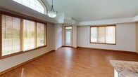 This single-floor residence offers a thoughtfully designed layout that balances open living spaces with comfortable private quarters. The main living and dining area is defined by soaring vaulted ceilings and an abundance of natural light streaming through multiple large windows fitted with wood-framed blinds. Warm hardwood-style flooring flows throughout the main living areas, complemented by a stylish pendant light fixture that anchors the space.

The kitchen is positioned at the heart of the home, featuring stainless steel appliances — including a refrigerator with ice maker, a range, and a built-in microwave — paired with warm wood cabinetry and a granite-topped breakfast bar that provides additional seating and workspace. Recessed lighting illuminates the kitchen and living area, enhancing the open, airy atmosphere created by the vaulted ceiling.

The bedroom is generously sized, finished with plush wall-to-wall carpeting and a tray ceiling detail that adds architectural interest. It benefits from natural light through a window with blinds and offers direct access to both an en-suite bathroom and a spacious walk-in closet. The bathroom features warm wood cabinetry with ample drawer storage, a white countertop, a large mirror, and a combination tub and shower with a sliding glass door. The walk-in closet is equipped with multiple wire shelving units and hanging rods, providing excellent storage capacity.