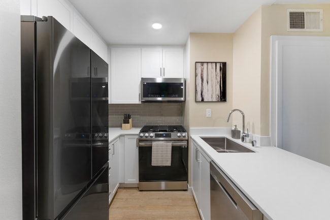 Renovated Package II kitchen with stainless steel appliances, white quartz countertops, white cabinetry, grey tile backsplash, and hard surface flooring - Avalon Burbank