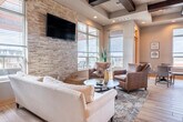 Located at 489 Commerce Dr in Madison, WI, this thoughtfully designed single-floor space seamlessly integrates a living room, dining area, and kitchen into one cohesive open-plan layout. The most striking architectural feature is the richly stained dark wood coffered ceiling, which adds depth, warmth, and a sense of grandeur to the entire space.

The living area is anchored by a textured stone accent wall with a wall-mounted television, flanked by large windows that flood the room with natural light and offer views of the surrounding neighborhood. Light wood-tone flooring runs throughout, complementing the warm neutral palette of the walls.

The kitchen is well-equipped with rich dark wood cabinetry, stone tile backsplash, stainless steel appliances, and granite countertops. A breakfast bar provides additional seating and connects the kitchen directly to the dining area, making the space ideal for both everyday use and entertaining.

The dining area features a round table with comfortable seating, positioned near large windows that continue the theme of natural light throughout. Decorative floating shelves adorn the walls, adding character and visual interest. A separate windowed nook near a sliding glass door offers a bright transition point with outdoor views, enhancing the open, airy feel of this well-designed space.