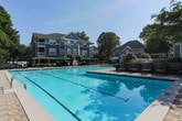 Located in Atlanta, GA (30339), this fitness and recreation facility offers a well-rounded array of amenities designed to support an active lifestyle. The centerpiece of the outdoor area is a generously sized swimming pool with clear turquoise water, surrounded by a paved pool deck furnished with lounge chairs and teal umbrella-shaded seating areas. Mature trees frame the space, providing shade and a pleasant natural backdrop alongside the multi-story residential building.

The interior fitness space is thoughtfully laid out across a single floor and features light hardwood flooring throughout, lending a clean and bright aesthetic. Large windows and glass-paneled French doors flood the rooms with abundant natural light and offer views of the surrounding grounds. Elevated transom windows further enhance the airy atmosphere.

The functional training room is equipped with wall-mounted TRX suspension straps and additional anchor points, making it well-suited for bodyweight and resistance-based workouts. An adjoining studio area houses spin bikes, a wall-mounted flat-screen television, and a stability ball, ideal for group or individual cardio sessions. A dedicated rack of colorful free weights adds versatility to the space. Crown molding and neutral gray walls contribute to a polished, well-maintained environment throughout.