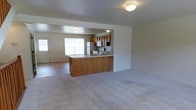 This three-floor home offers a functional and welcoming layout designed for comfortable everyday living. The main level showcases an open-concept design where the living area flows seamlessly into the kitchen, creating a connected and spacious feel. The kitchen is equipped with warm honey-toned wood cabinetry, a full suite of appliances including a refrigerator, microwave, and range, and features a peninsula with a light countertop that provides additional prep space and serves as a natural divider between the cooking and living zones. Soft, neutral-toned carpet covers the living area floors, adding warmth and comfort underfoot. Natural light filters into the space through a prominent window in the living area, brightening the room and creating an airy atmosphere. A secondary entry door is also visible, offering convenient access. The neutral wall tones and understated finishes throughout give the home a clean, move-in-ready appearance. Spread across three floors, this home provides ample room for living, sleeping, and storage, making it a versatile and practical space suited to a variety of lifestyles.