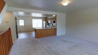This three-floor home offers a functional and welcoming layout designed for comfortable everyday living. The main level showcases an open-concept design where the living area flows seamlessly into the kitchen, creating a connected and spacious feel. The kitchen is equipped with warm honey-toned wood cabinetry, a full suite of appliances including a refrigerator, microwave, and range, and features a peninsula with a light countertop that provides additional prep space and serves as a natural divider between the cooking and living zones. Soft, neutral-toned carpet covers the living area floors, adding warmth and comfort underfoot. Natural light filters into the space through a prominent window in the living area, brightening the room and creating an airy atmosphere. A secondary entry door is also visible, offering convenient access. The neutral wall tones and understated finishes throughout give the home a clean, move-in-ready appearance. Spread across three floors, this home provides ample room for living, sleeping, and storage, making it a versatile and practical space suited to a variety of lifestyles.