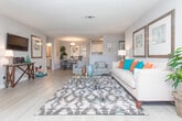 This single-floor residence offers a thoughtfully designed layout with a seamless flow between its key living spaces. The spacious living room features wood-look flooring, a ceiling fan, and large windows that invite an abundance of natural light, creating a bright and welcoming atmosphere. Adjacent to the living area, the dining space is defined by elegant framed wall art and a modern pendant light fixture overhead, making it an ideal setting for both casual meals and entertaining.

The galley-style kitchen is well-equipped, boasting white cabinetry with brushed nickel hardware, stone-look countertops, a deep double-basin stainless steel sink, and stainless steel appliances. A passthrough view connects the kitchen directly to the dining area, enhancing the open feel of the home.

The bedroom is a comfortable retreat, carpeted for warmth and featuring generous windows that provide ample natural light and outdoor views. Two bathrooms serve the residence — one with a vanity featuring a round sink and stone-look countertop with a large framed mirror, and another with a full tub-shower combination with tile surround.

A dedicated laundry room with a full-size washer and dryer adds everyday convenience. Neutral tones and wood-look flooring throughout the main areas tie the residence together with a cohesive, modern aesthetic.