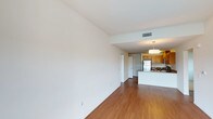 Located at 320 Town Center Pkwy in Santee, this single-floor unit offers a clean, open-concept layout that seamlessly connects the living area to the kitchen. The living space is finished with warm hardwood-style flooring and crisp white walls, creating a bright and neutral canvas well-suited for a variety of interior styles. Natural light flows through the space, enhancing its airy feel.

The kitchen is a standout feature, outfitted with light wood cabinetry, stainless steel appliances including a refrigerator and microwave, and a peninsula counter that doubles as a breakfast bar or workspace. A modern pendant light fixture anchors the kitchen area, adding a touch of contemporary style. The countertops provide ample prep and storage space, making the kitchen both functional and visually appealing.

Recessed and overhead lighting is integrated throughout, ensuring consistent illumination across the open floor plan. A central HVAC vent is visible in the ceiling, indicating climate control throughout. A doorway visible from the main living area leads to additional spaces within the unit. The overall ambiance is clean, modern, and move-in ready, offering a versatile and well-appointed living environment in the heart of Santee.