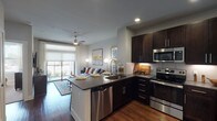 This 1-bedroom, 1-bathroom residence is designed with a contemporary open-concept layout that seamlessly connects the kitchen, dining, and living areas. The kitchen is a standout feature, boasting rich dark-espresso cabinetry that extends to the ceiling for ample storage, sleek quartz countertops, a peninsula island ideal for casual dining, and a full suite of stainless steel appliances including a French door refrigerator, electric range, built-in microwave, and dishwasher. Warm hardwood-style flooring flows throughout the main living areas, adding both visual warmth and cohesion to the space. The living room is bright and inviting, anchored by a ceiling fan and a large sliding glass door that opens onto a private balcony, filling the room with natural light and outdoor views. The bedroom is a comfortable retreat with plush carpeting, large windows that invite natural light, and a ceiling fan for year-round comfort. The full bathroom features a wide dark-cabinetry vanity with a quartz countertop, an undermount sink, and a large framed mirror, with direct access to a spacious walk-in closet equipped with built-in shelving and hanging rods. A stacked in-unit laundry is also included, adding everyday convenience to this thoughtfully designed home.