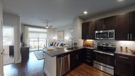 This 1-bedroom, 1-bathroom residence is designed with a contemporary open-concept layout that seamlessly connects the kitchen, dining, and living areas. The kitchen is a standout feature, boasting rich dark-espresso cabinetry that extends to the ceiling for ample storage, sleek quartz countertops, a peninsula island ideal for casual dining, and a full suite of stainless steel appliances including a French door refrigerator, electric range, built-in microwave, and dishwasher. Warm hardwood-style flooring flows throughout the main living areas, adding both visual warmth and cohesion to the space. The living room is bright and inviting, anchored by a ceiling fan and a large sliding glass door that opens onto a private balcony, filling the room with natural light and outdoor views. The bedroom is a comfortable retreat with plush carpeting, large windows that invite natural light, and a ceiling fan for year-round comfort. The full bathroom features a wide dark-cabinetry vanity with a quartz countertop, an undermount sink, and a large framed mirror, with direct access to a spacious walk-in closet equipped with built-in shelving and hanging rods. A stacked in-unit laundry is also included, adding everyday convenience to this thoughtfully designed home.