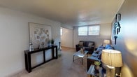 This single-floor unit offers a comfortable and functional layout across several distinct living spaces. The living room is generously proportioned, featuring neutral carpet flooring, a textured ceiling, and multiple windows that bring in natural light. The open seating arrangement accommodates both a full sofa and loveseat, creating a welcoming gathering space.

The kitchen is equipped with dark cabinetry, black appliances including a range, dishwasher, and refrigerator, and light-toned countertops. Wood-look flooring runs through the kitchen and into the adjacent dining area, where a ceiling fan overhead and a window with blinds add to the casual, functional atmosphere. The dining nook comfortably fits a pub-height table and stools.

The primary bedroom features carpet flooring, a closet, and warm ambient lighting, with ample space for a full-sized bed and furnishings. The second bedroom, also carpeted, is equally well-sized and benefits from natural light through a window with blinds. Both rooms offer a calm, restful atmosphere.

The bathroom includes wood-look flooring, a shower-tub combination, and a clean, straightforward layout. Throughout the unit, the design is cohesive and practical, reflecting a comfortable residential living environment.