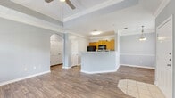 This single-story residence is designed with an open, flowing layout that connects the main living areas seamlessly. The living room is a standout space, featuring an elevated tray ceiling accented with crown molding and a ceiling fan, flanked by large windows and a glass-panel exterior door that fills the room with natural light and provides access to an outdoor area. Wood-look flooring runs throughout the main living and kitchen spaces, lending warmth and continuity.

The kitchen is positioned behind a prominent peninsula that serves as both a workspace and a casual bar. Warm honey-toned oak cabinetry lines the walls from floor to ceiling, complemented by light granite-style countertops and a full suite of black appliances, including a refrigerator, range, built-in microwave, and dishwasher. An arched entryway near the kitchen leads to additional rooms, adding an architectural detail that softens the otherwise clean-lined interior.

The bedrooms are carpeted and well-lit by sizeable windows with outdoor greenery views, each equipped with ceiling fans and ample closet space. The bathroom features a warm oak vanity with generous drawer storage, a granite-style countertop, a wide wall mirror, and a shower-tub combination. Throughout, the soft gray wall palette creates a calm, neutral ambiance.