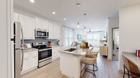 Located at 1250 Marden Rd in Apopka, FL, this thoughtfully designed one-bedroom, one-bathroom residence offers a cohesive open-concept floor plan that maximizes every square foot. The kitchen is a standout feature, showcasing crisp white shaker cabinetry, granite countertops, stainless steel appliances, a built-in wine rack, a subway tile backsplash, and a central island with bar seating — all illuminated by recessed and pendant lighting. Light wood-style flooring flows seamlessly through the kitchen, dining, and living areas, enhancing the airy, connected feel of the space. The dining area accommodates a full table beneath an elegant drum pendant light, while large windows flood the room with natural light. The living room offers access to a private balcony and features floor-to-ceiling drapes, a ceiling fan, and ample space for comfortable seating. The bedroom is carpeted and well-lit by large windows, offering a serene retreat with a dedicated closet. The bathroom presents a clean, spa-like aesthetic with a dual-sink granite vanity, backlit mirrors, white cabinetry, and wood-look flooring. Throughout, the space maintains a bright, modern, and welcoming ambiance.