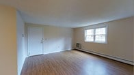 This single-floor, 2-bedroom, 1-bathroom residence is designed with simplicity and functionality in mind. The living area greets you with warm hardwood-style flooring that extends throughout, complemented by clean, neutral-toned walls that create a bright and welcoming atmosphere. A large window allows generous natural light to fill the room while offering a view of the surrounding greenery outside. A wall-mounted air conditioning unit and baseboard heating ensure year-round comfort. The front entry door opens directly into the main living space, providing a straightforward and open layout. The understated design provides a versatile canvas, allowing residents to personalize the interior to their preferences. The two bedrooms offer comfortable private retreats, while the bathroom serves the household with practical convenience. The overall layout is efficient, making thoughtful use of the available space across the single floor. This residence is well-suited for those seeking a straightforward, move-in-ready home with essential amenities and a clean, unpretentious aesthetic.
