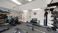 Located at 1160 Auston Grove Rd in Raleigh, NC, this well-appointed fitness center offers a comprehensive workout environment designed to accommodate a wide range of exercise needs. The single-floor facility features soaring vaulted ceilings accented by crown molding, lending the space an open and airy feel. Durable rubber flooring throughout provides both safety and comfort during workouts.

The cardio zone is outfitted with multiple treadmills and elliptical trainers, complemented by a wall-mounted flat-screen TV and a large mirror that visually expands the space. A recumbent bike and cable weight machine round out the strength and cardio offerings. Natural light pours in through a bank of large windows fitted with blinds, offering pleasant views of the surrounding greenery.

The free weights area includes a full dumbbell rack, a stability ball, and a weight bench with a barbell, providing ample options for resistance training. A dedicated functional training zone features a TRX-style multi-use rack stocked with medicine balls, kettlebells, resistance bands, and a heavy punching bag. Elegant French doors connect to an adjacent space, adding a refined architectural touch. Bright recessed and flush-mount lighting ensures excellent visibility throughout the facility.