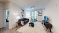 Located at 222 N West St in the heart of downtown Raleigh, NC, this thoughtfully designed 2-bedroom, 2-bathroom residence offers a clean, contemporary aesthetic throughout. The open-concept living area seamlessly connects the kitchen, dining, and living spaces, all finished with warm wood-look flooring and crisp white walls. The modern kitchen is a standout feature, boasting a large center island with quartz countertops, white cabinetry, stainless steel appliances, and globe pendant lighting that adds a stylish focal point. The living and dining area is bathed in natural light from full-length windows and a glass door leading to a private balcony. Both bedrooms are well-appointed, featuring ceiling fans, large windows, and generous closet space. The primary suite includes a spacious walk-in closet with custom built-in shelving and drawers. The en-suite bathroom offers a dual-sink vanity with a backlit mirror and a glass-enclosed tile shower. The second bathroom mirrors the same refined finishes. Additional highlights include multiple closets, a dedicated laundry area, and a utility room, ensuring ample storage throughout. The overall ambiance is light, airy, and move-in ready.
