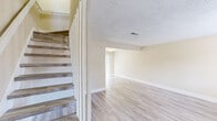 This two-story townhouse in Slidell, Louisiana, offers a practical and well-organized layout spread across two levels. The main floor features an open living area finished with light-toned luxury vinyl plank flooring that runs consistently throughout the home, complementing the neutral beige walls and white baseboards. A staircase with wood-toned treads connects the two floors, positioned adjacent to the living space. The living area receives natural light through a sliding glass door fitted with vertical blinds, opening to a fenced backyard. A pass-through counter separates the living area from the kitchen, which is configured in a U-shape with white cabinetry, warm-toned laminate countertops, a double stainless steel sink, and a window above that brings in additional natural light. Textured ceilings are present throughout the main level.

The two bedrooms each feature the same LVP flooring, ceiling fans with light fixtures, and neutral walls. One bedroom includes a sliding closet, while another offers a natural view through a window with blinds. The two full bathrooms include one with a tub-shower combination and another with a standalone shower unit featuring built-in shelving. HVAC vents are present in multiple rooms.