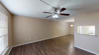 This single-story residence offers a practical and comfortable layout across two bedrooms and one bathroom. The living area greets you upon entry through a paneled front door, featuring rich, dark wood-look flooring and a ceiling fan with integrated lighting. Natural light enters through a window fitted with blinds, creating a welcoming atmosphere. An adjacent dining area is defined by a pendant light fixture, continuing the same durable flooring throughout.

The galley-style kitchen is efficiently arranged with white cabinetry on both sides, dark laminate countertops, a double-basin stainless steel sink, and white appliances including a range, dishwasher, and refrigerator. Light tile flooring and overhead cabinetry extending to the ceiling maximize storage capacity.

Both bedrooms are carpeted and equipped with ceiling fans and natural light from windows with blinds. One bedroom features direct access to the hallway and a view toward the bathroom and laundry area. The shared full bathroom includes a tub and shower combination with large-format, marble-look tile surround, brushed nickel fixtures and hardware, and tile flooring, offering a clean and updated appearance.
