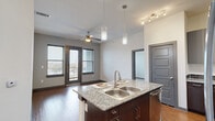 Located in Denton, TX, this well-appointed 4-bedroom, 2-bathroom unit offers a functional and modern layout across a single floor. The open-concept kitchen and living area serves as the heart of the home, featuring a central island with granite countertops and a double stainless steel sink, accented by stylish pendant lighting. The kitchen is further equipped with gray upper cabinetry, a tile backsplash, and a full suite of stainless steel appliances including a range, microwave, and refrigerator. Rich hardwood-style flooring flows throughout the main living areas, while a ceiling fan and glass-paneled door leading to an outdoor space add to the living room's comfort and natural light. The four bedrooms are carpeted and offer a calm, neutral palette, each with access to dedicated closets and connected via a central hallway with dark-trimmed panel doors. Both bathrooms feature full soaking tubs with floor-to-ceiling gray tile surrounds, granite vanity tops, dark wood cabinetry, and hardwood-style flooring. A dedicated laundry area houses a full-size washer and dryer with overhead shelving, adding everyday convenience to this thoughtfully designed home.