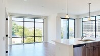 This thoughtfully designed two-bedroom, two-bathroom unit at 31 Holland Ave in Albany, New York offers a modern aesthetic defined by clean lines, light wood-toned flooring, and an abundance of natural light. The open-concept living, dining, and kitchen area forms the heart of the unit, where expansive floor-to-ceiling windows with bold black frames frame sweeping views of the surrounding cityscape and tree canopy. A balcony is accessible directly from the living area, extending the sense of openness. The kitchen is well-appointed with grey wood-finish cabinetry extending to the ceiling, stainless steel appliances including a range, microwave, and French door refrigerator, and a white quartz-topped island that provides additional workspace and seating.

Both bedrooms are carpeted and bathed in natural light through large black-framed windows offering outdoor views. The primary bedroom features floor-to-ceiling glazing, reinforcing the unit's airy character. The two bathrooms are finished in a clean, minimalist style — one includes a walk-in shower, while the other features a soaking tub. Light wood-toned flooring runs throughout the main living spaces, contributing to the unit's cohesive, contemporary feel.