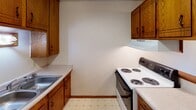 This single-floor unit offers a straightforward, functional layout across several well-defined spaces. The kitchen is equipped with warm oak cabinetry providing ample upper and lower storage, a coil-burner electric range with an overhead ventilation hood, and a single-basin sink set into light-toned countertops. Vinyl tile flooring with a classic diamond pattern adds a practical, easy-to-clean surface underfoot.

The living area features neutral carpet and transitions into a tiled entryway zone, illuminated by a flush-mount ceiling fixture. A sliding glass door opens to a private balcony, offering views of surrounding greenery and allowing natural light to fill the space. A wall-mounted air conditioning unit and baseboard heating provide year-round climate control.

Two bedrooms are carpeted and each include sliding-door closets with hanging rods and shelving. One bedroom benefits from a ceiling fan with light fixture and a window overlooking greenery, while the other features a spacious closet and baseboard heater. Both rooms display textured ceilings throughout.

The bathroom includes a pink-toned tub and tile surround, a toilet, a single vanity with under-sink storage, and pink mosaic tile flooring — reflecting a classic, retro aesthetic consistent with the unit's overall character.