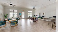 This well-appointed office suite occupies a single floor and is thoughtfully designed to balance professional functionality with an inviting, contemporary aesthetic. Light hardwood flooring runs throughout the space, complementing the bright white walls and crown molding that lend a polished, cohesive feel.

The main open-plan office area is generously proportioned, featuring high ceilings with ceiling fans, large windows with transom lights above, and glass-paned French doors that flood the space with natural light and offer views of lush surrounding greenery. This area includes a central conference table, a dedicated computer workstation counter along one wall, and a comfortable lounge seating arrangement with teal accent chairs, creating a versatile environment for both collaboration and focused work.

The second office is a more intimate, private space distinguished by soaring ceilings with clerestory windows and a warm wood desk paired with a lounge seating area featuring plush gray chairs. Curated abstract artwork adorns the walls throughout both offices, adding a refined artistic touch.

A welcoming reception or lounge area connects the two offices, outfitted with cognac leather accent chairs and soft neutral tones. The space benefits from ample natural light, a wall-mounted mini-split system, and thoughtful design details that create a calm, professional ambiance ideal for a modern office environment.